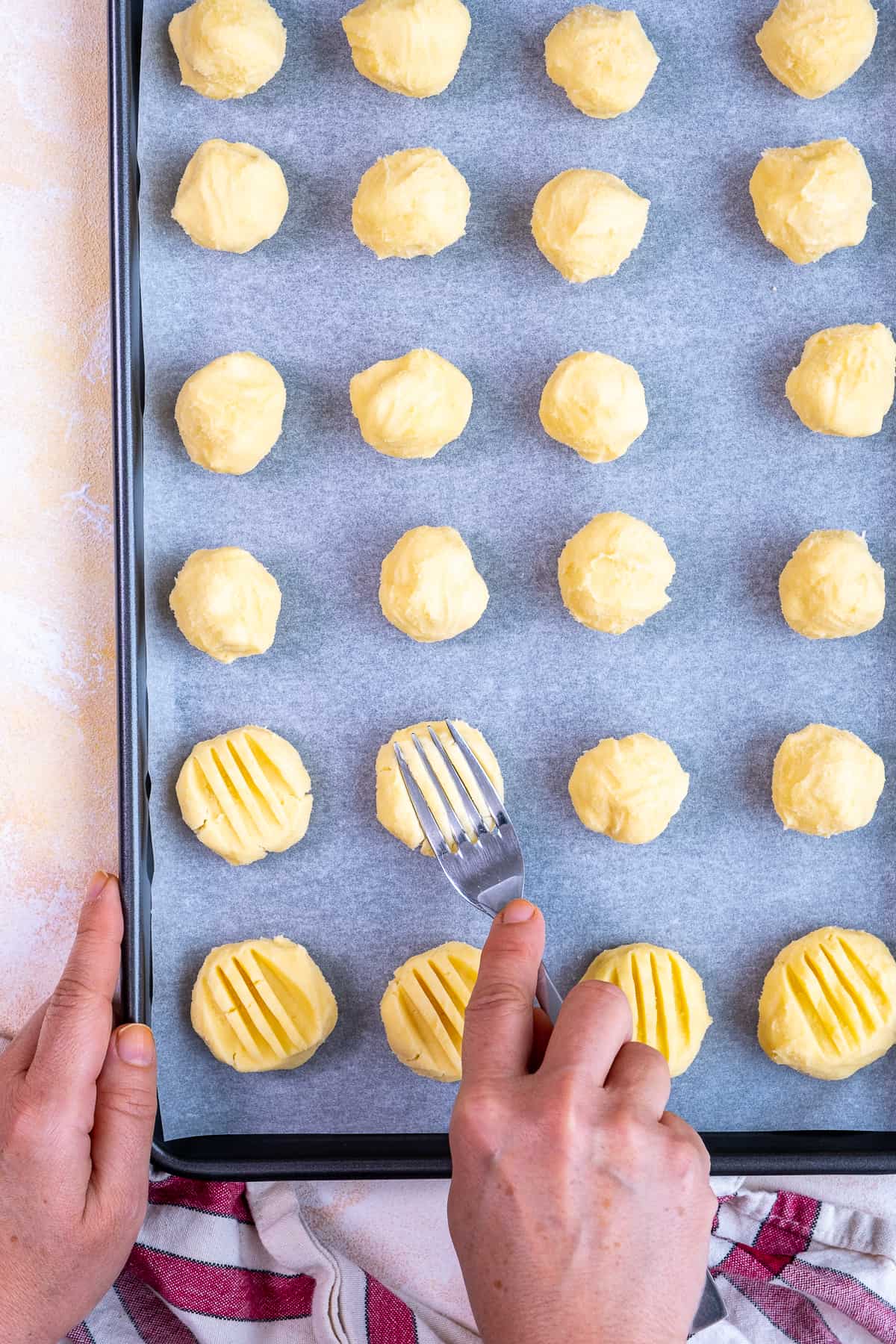 Hands pressing on cookie balls with a fork.