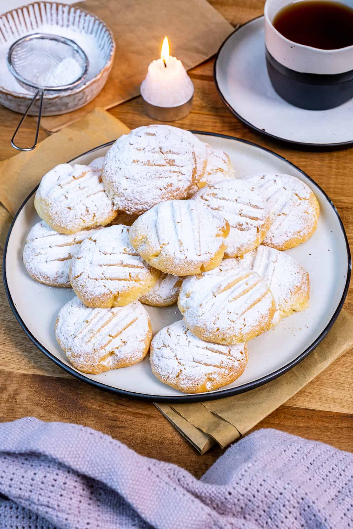 Cornflour cookies on a plate, a cup of tea, a small candle and powdered sugar on the side.