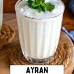 A close-up of a glass filled with foamy Turkish ayran, topped with mint, with text overlay reading “Ayran – Turkish Yogurt Drink” and the website “giverecipe.com” at the bottom.