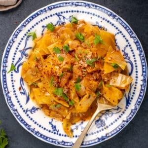 Kapuska in a white bowl, garnished with red pepper flakes and parsley and a spoon inside it.