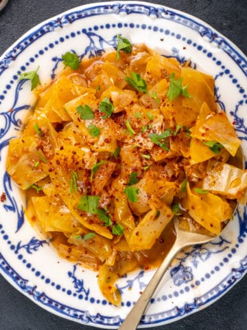 Kapuska in a white bowl, garnished with red pepper flakes and parsley and a spoon inside it.