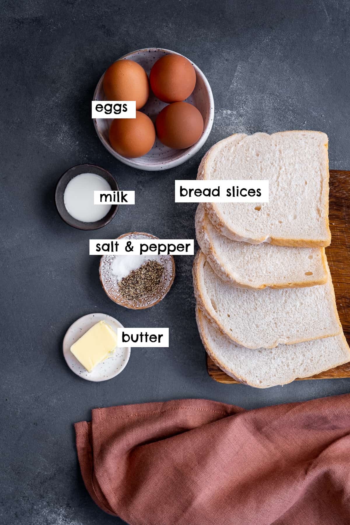 Bread slices, eggs, milk, butter, salt and pepper on a grey backdrop.