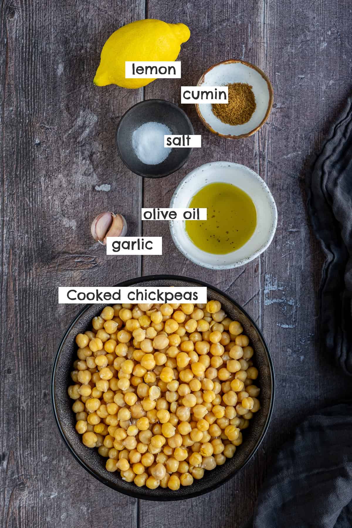 Cooked chickpeas, olive oil, garlic cloves, salt, cumin and lemon photographed from top view.