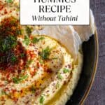 A close-up shot of hummus garnished with red pepper flakes, sumac, olive oil and fresh dill, with two pieces of torn flatbread dipped into it.