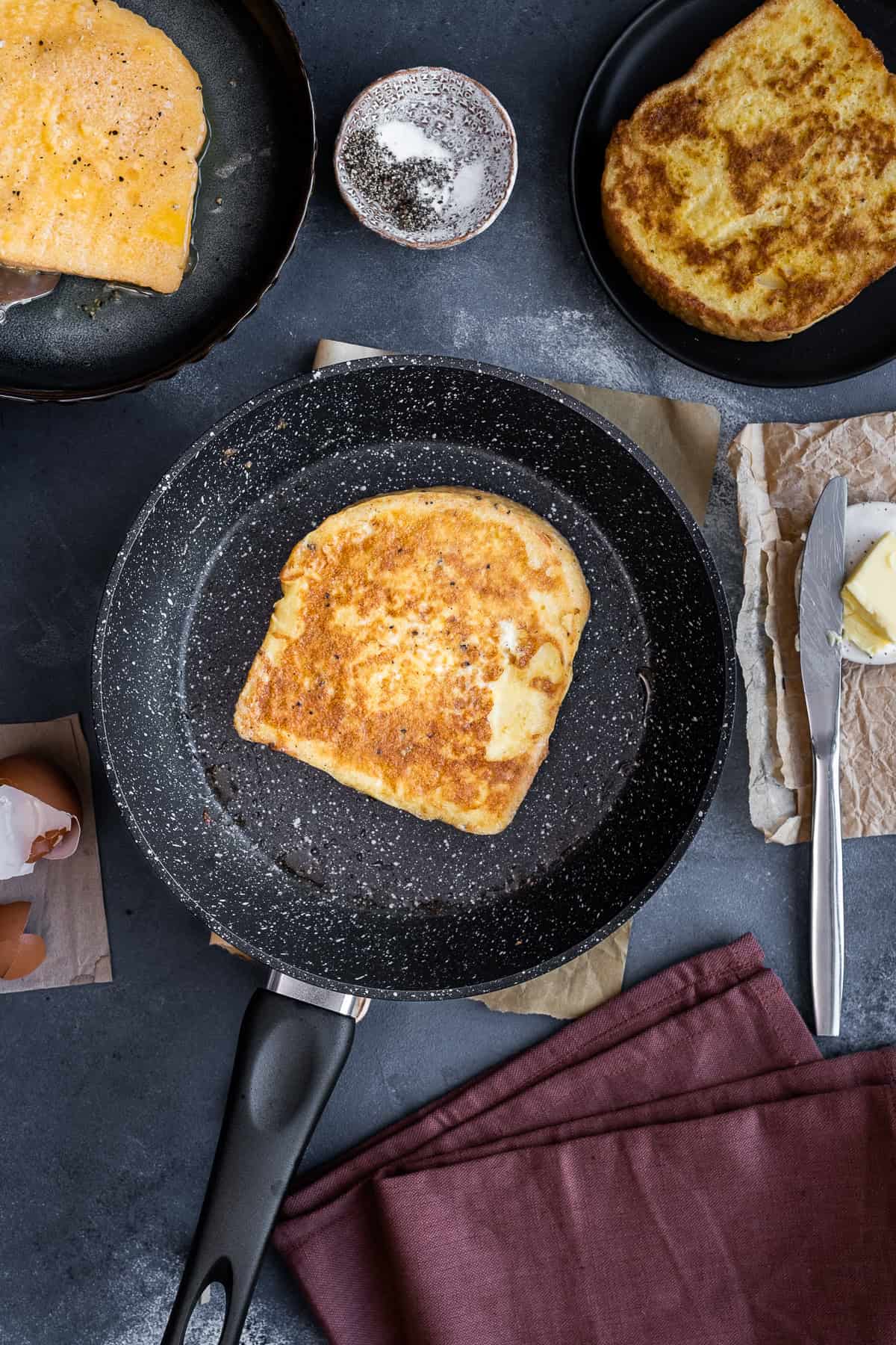 Turkish eggy bread (yumurtalı ekmek) frying in a pan, golden and crispy, with butter and seasoning on the side.