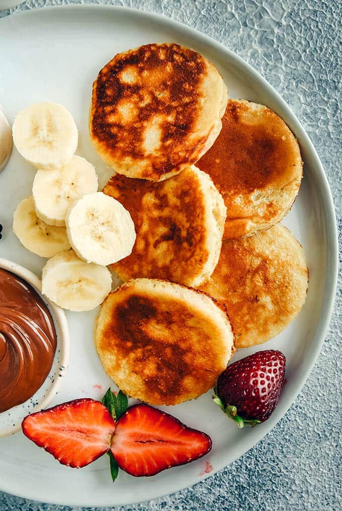 Banana yogurt pancakes with banana slices, strawberries and chocolate on a white plate 