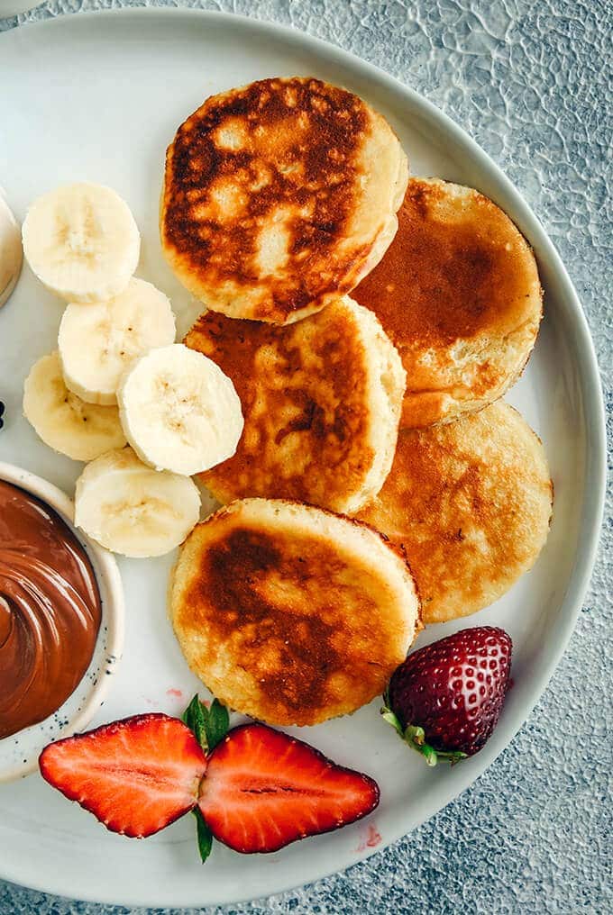 Banana yogurt pancakes with banana slices, strawberries and chocolate on a white plate