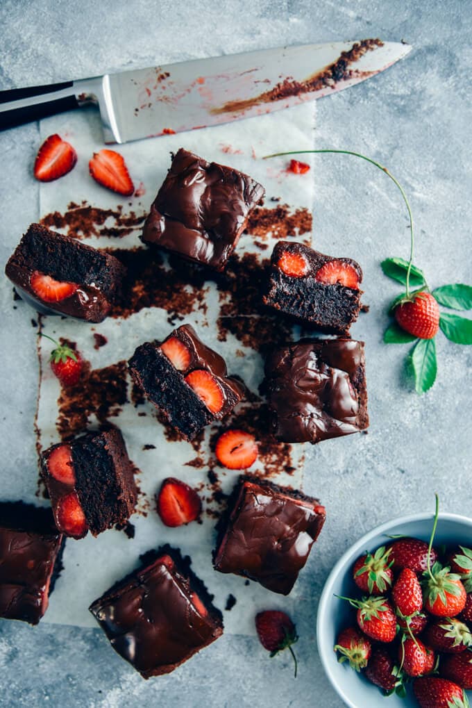 Chocolate-covered strawberry brownies on baking paper accompanied by fresh strawberries