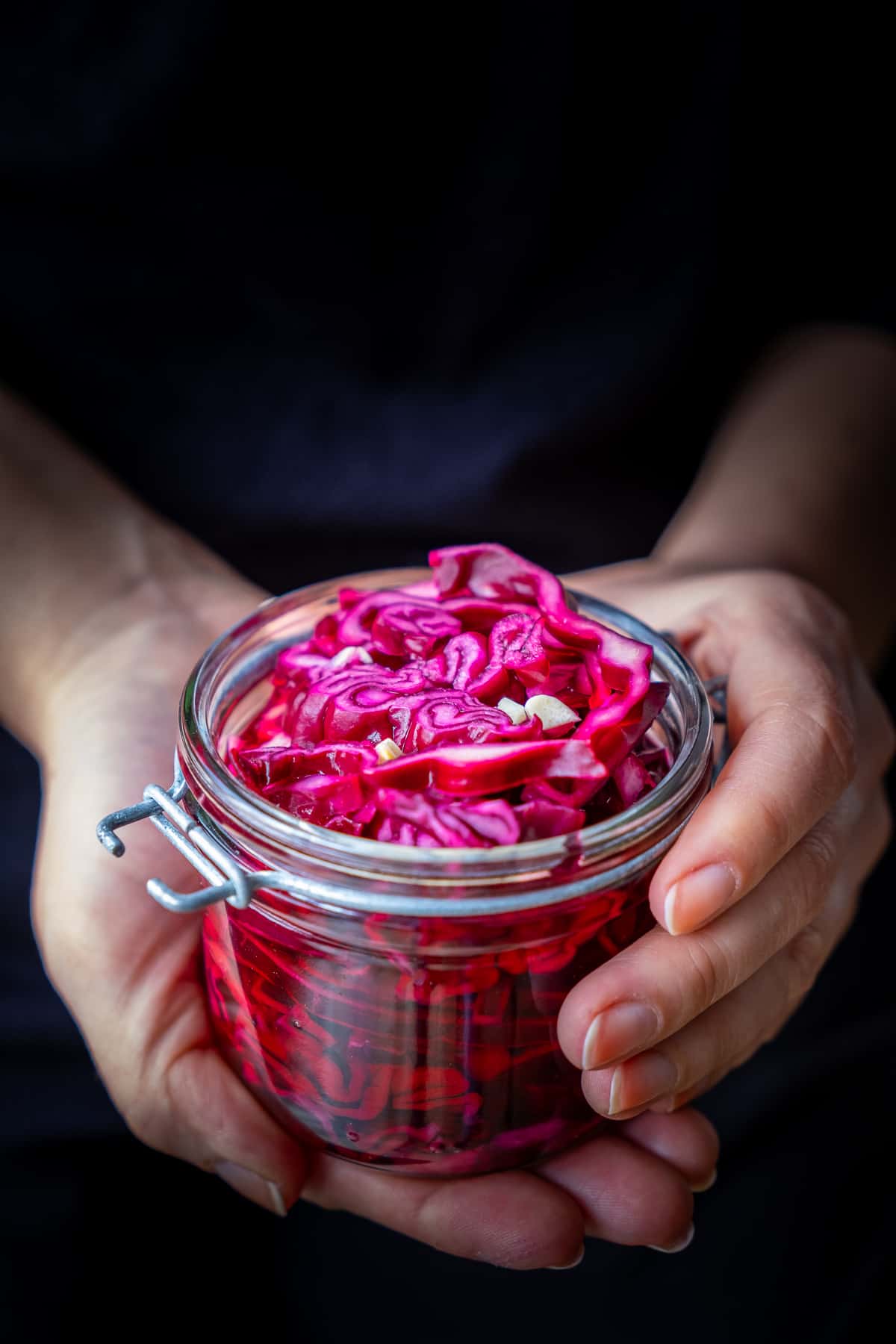 Hands holding a small jar of pickled red cabbage.