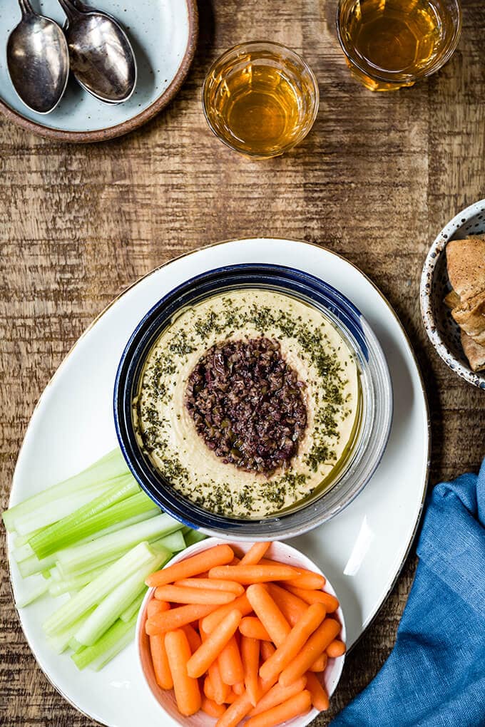 Hummus in a blue bowl served with raw veggies on the side