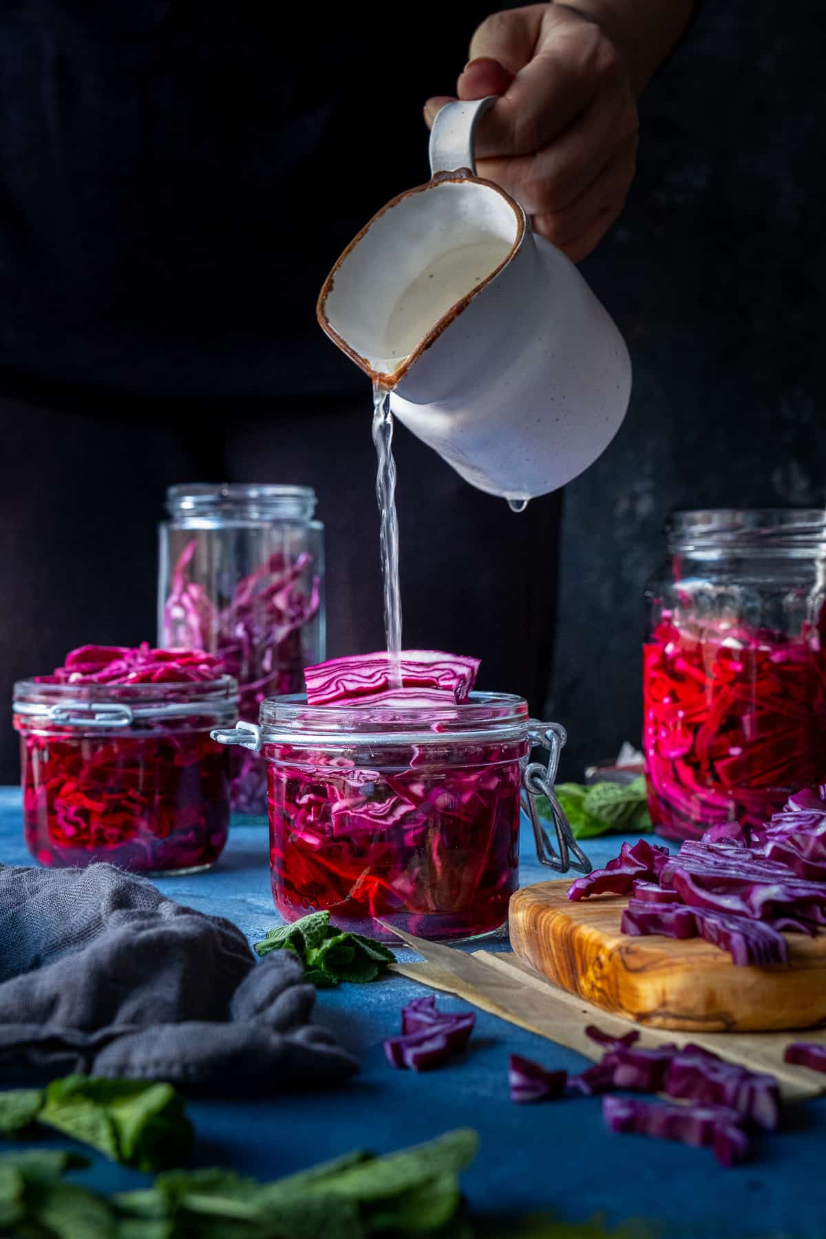 Pickle brine being poured over shredded red cabbage in a jar on a dark background.