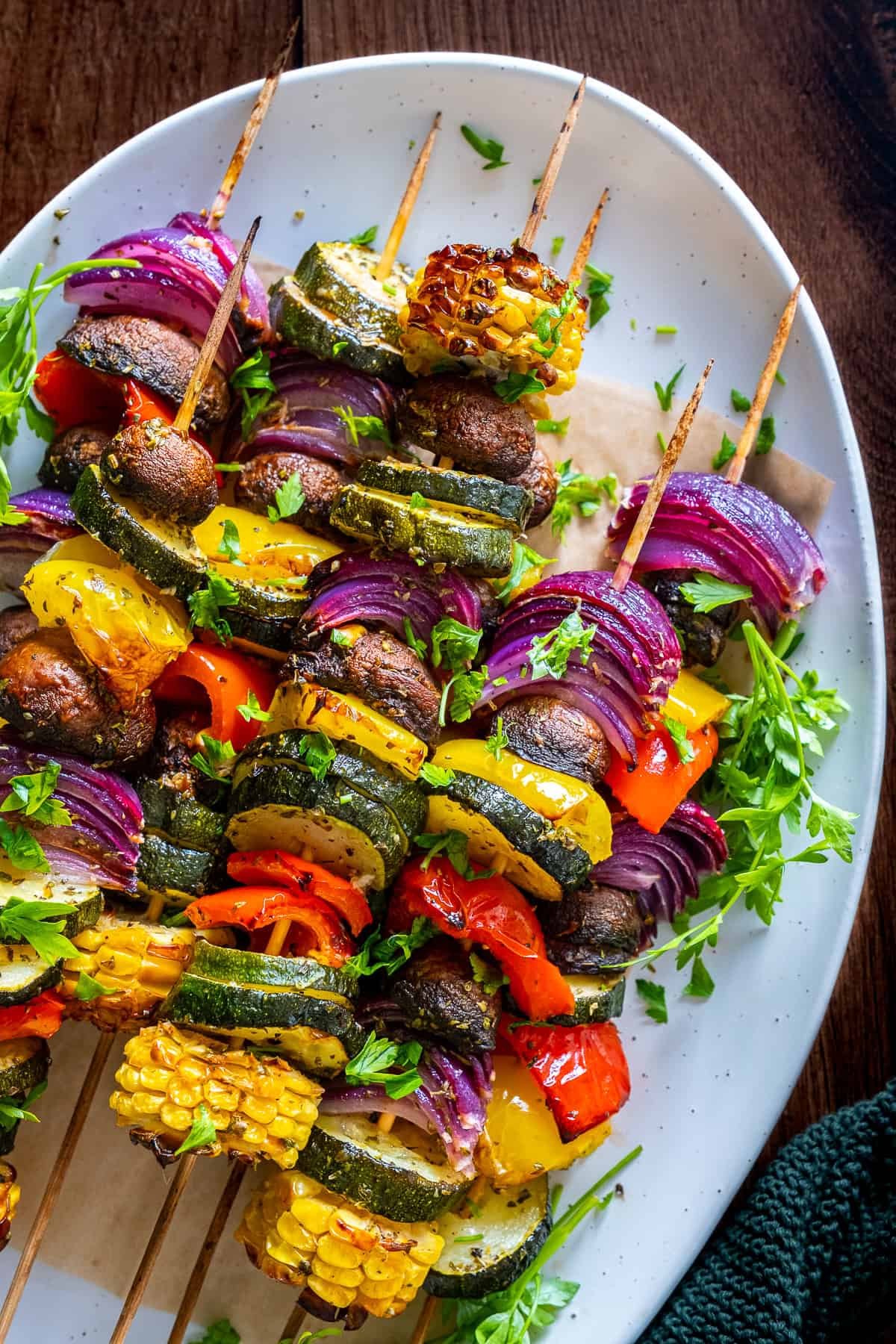 Close-up of colorful roasted vegetable kabobs with zucchini, mushrooms, red onion, peppers, and corn, served on skewers with fresh herb garnish.