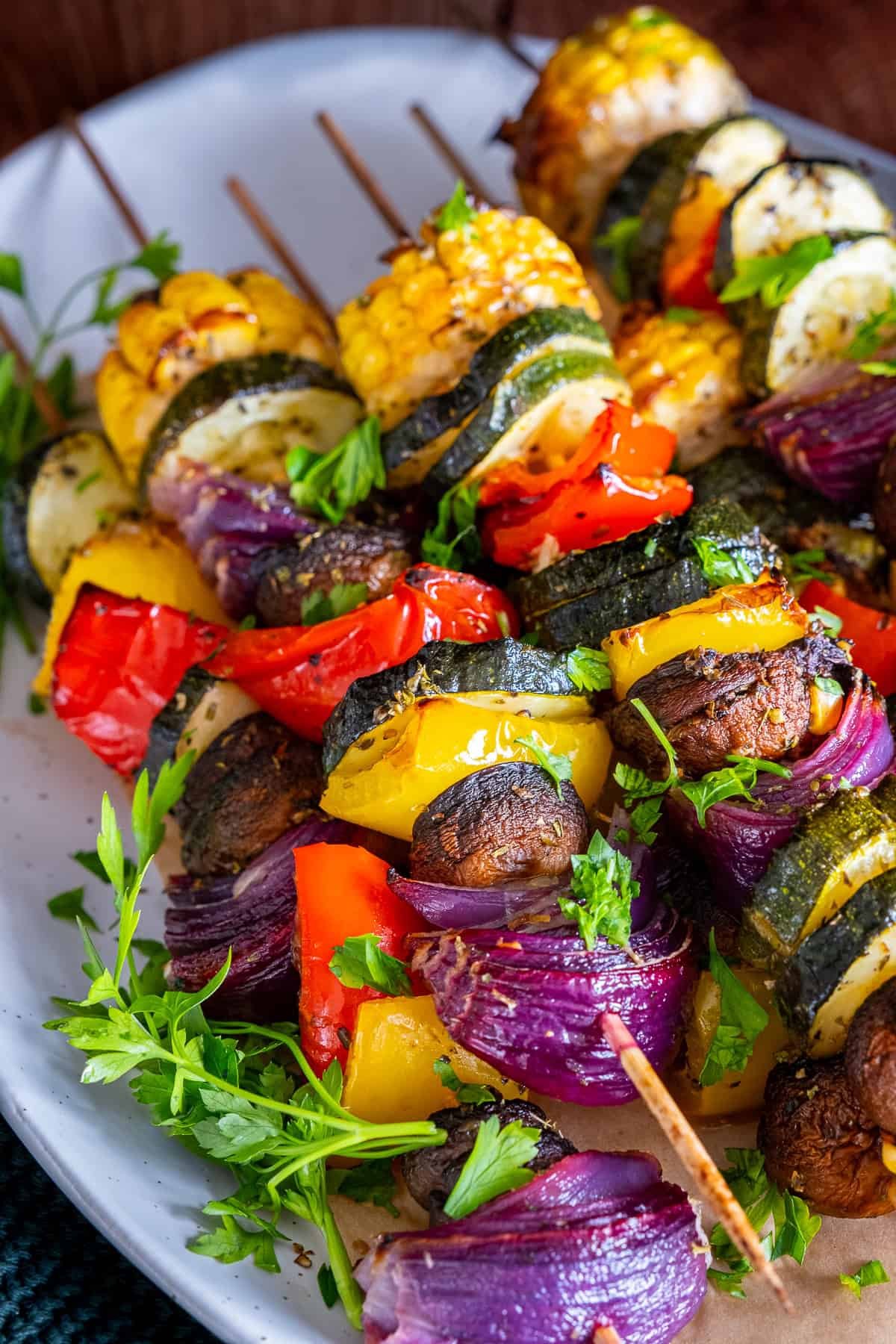 Close-up of oven-roasted vegetable kabobs with zucchini, red onion, corn, bell peppers, and mushrooms, garnished with fresh parsley.