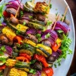 Oven-roasted vegetable kabobs with zucchini, mushrooms, bell peppers, red onions, and corn, garnished with parsley on a white plate.