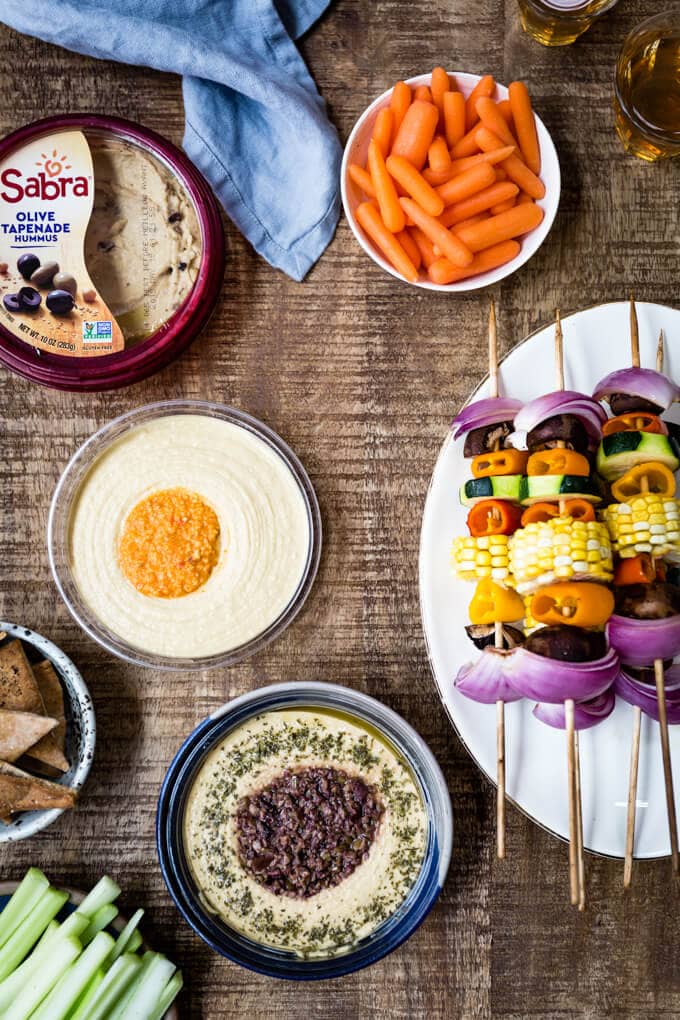 Vegetable shish kabob accompanied by hummus bowls and carrots on the side