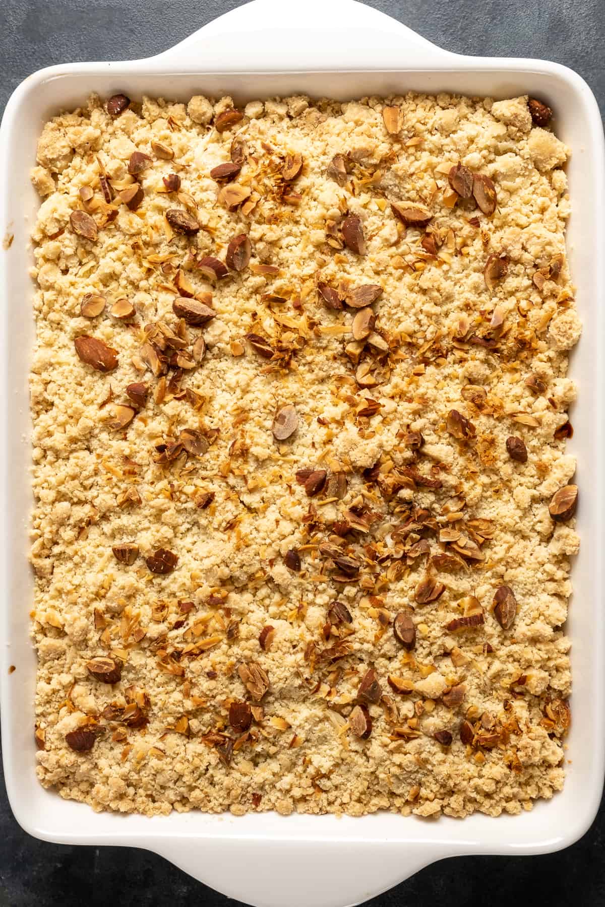 Peach cobbler with cake mix topped with almonds in a white baking pan.