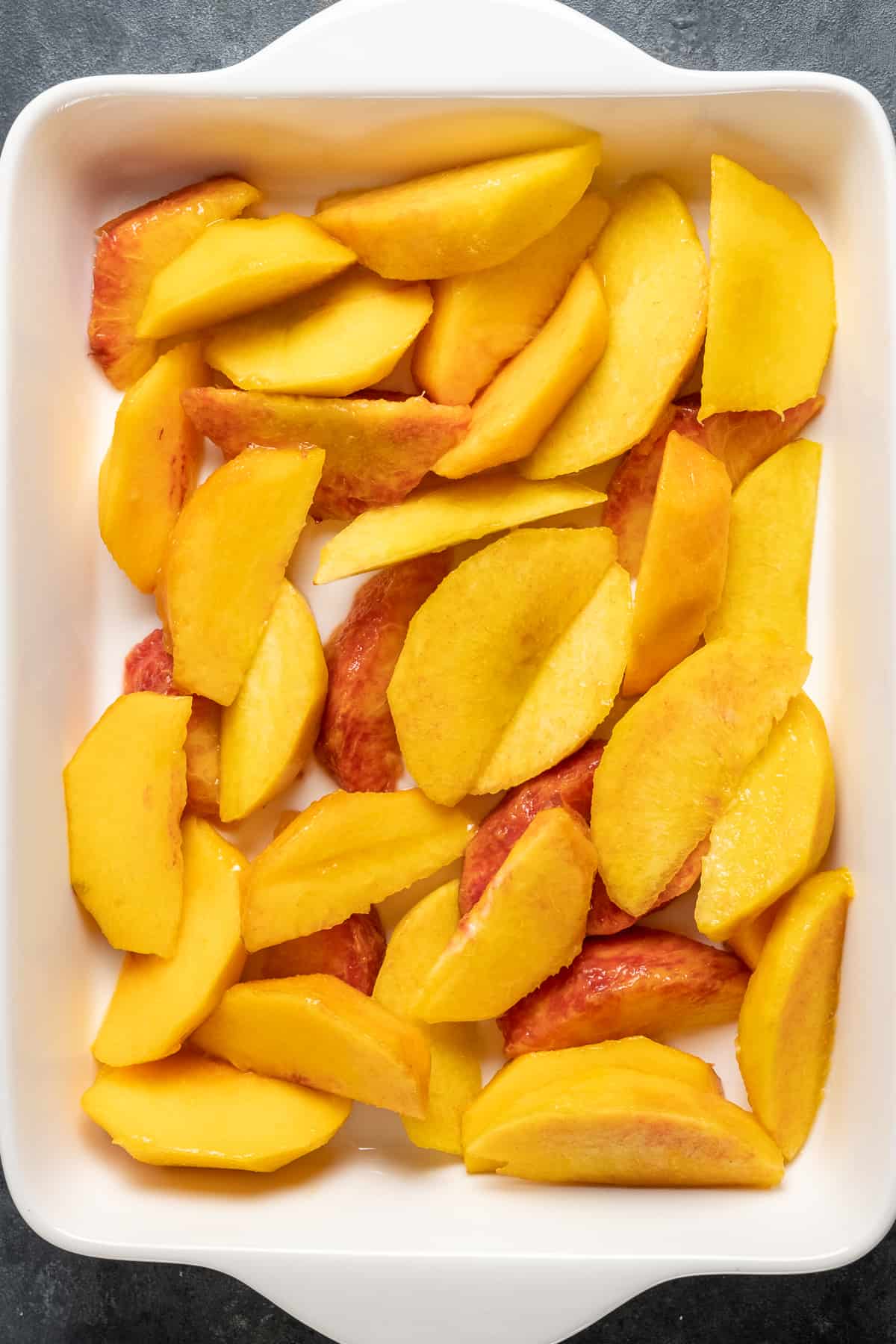 Peach slices covering the bottom of a white rectangular baking pan.