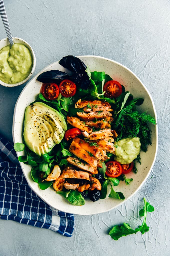 Keto chicken salad with avocado and herbs in a ceramic bowl on a grey background.