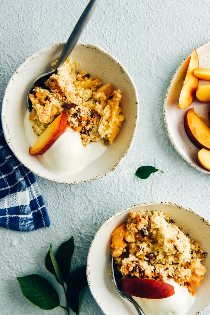 Peach cobbler with cake mix served in two white handmade ceramic bowls topped with vanilla ice cream and peach slices with a spoon on the side 