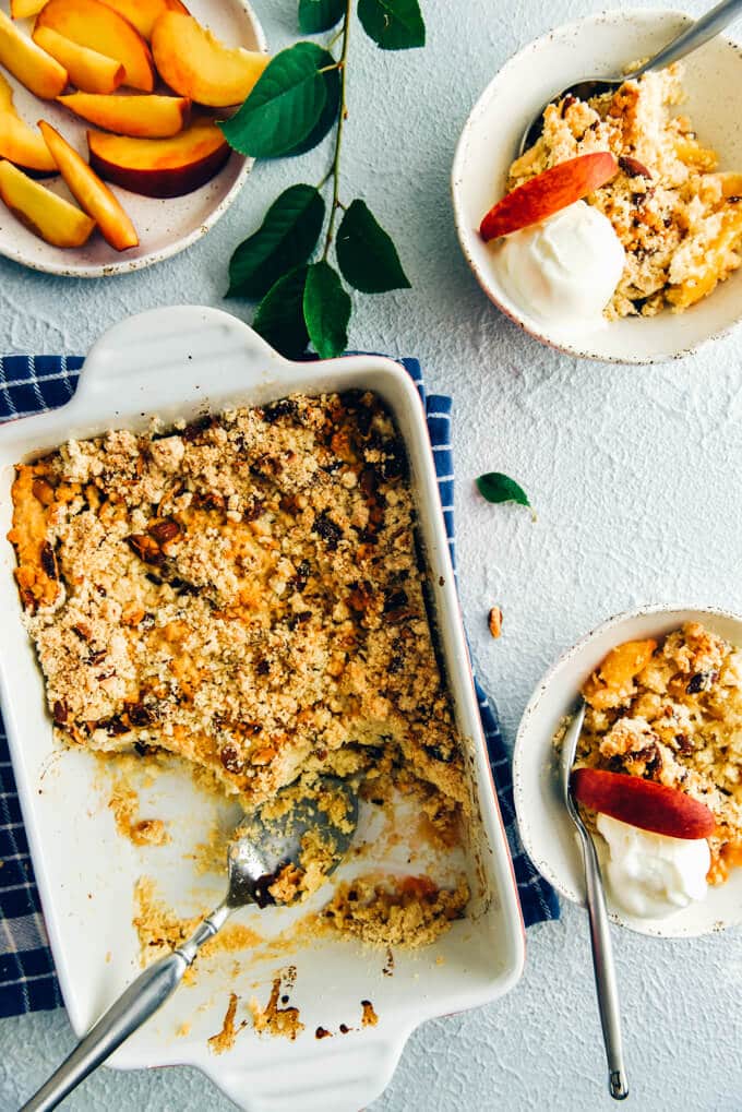 Peach cobbler made with cake mix in a rectangular baking pan and in two white ceramic bowls topped with vanilla ice cream and peach slices 