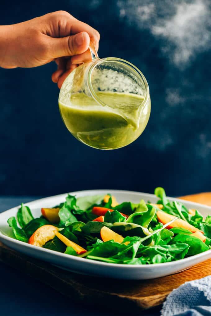 Pouring vegan avocado ranch dressing on a green salad