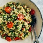 Vegan pasta salad with avocado dressing served in a handmade ceramic white bowl with two spoons on the side.