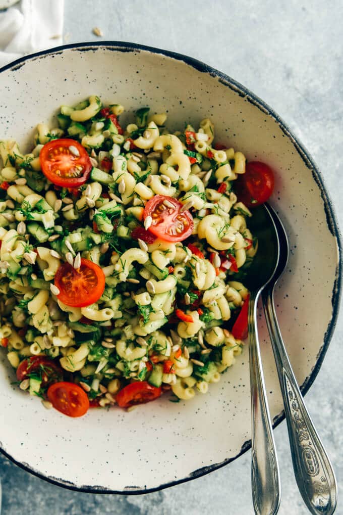 Vegan pasta salad with avocado dressing served in a handmade ceramic white bowl with two spoons on the side.