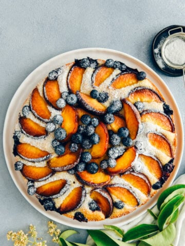 Blueberry peach coffee cake dusted with powdered sugar on a white plate