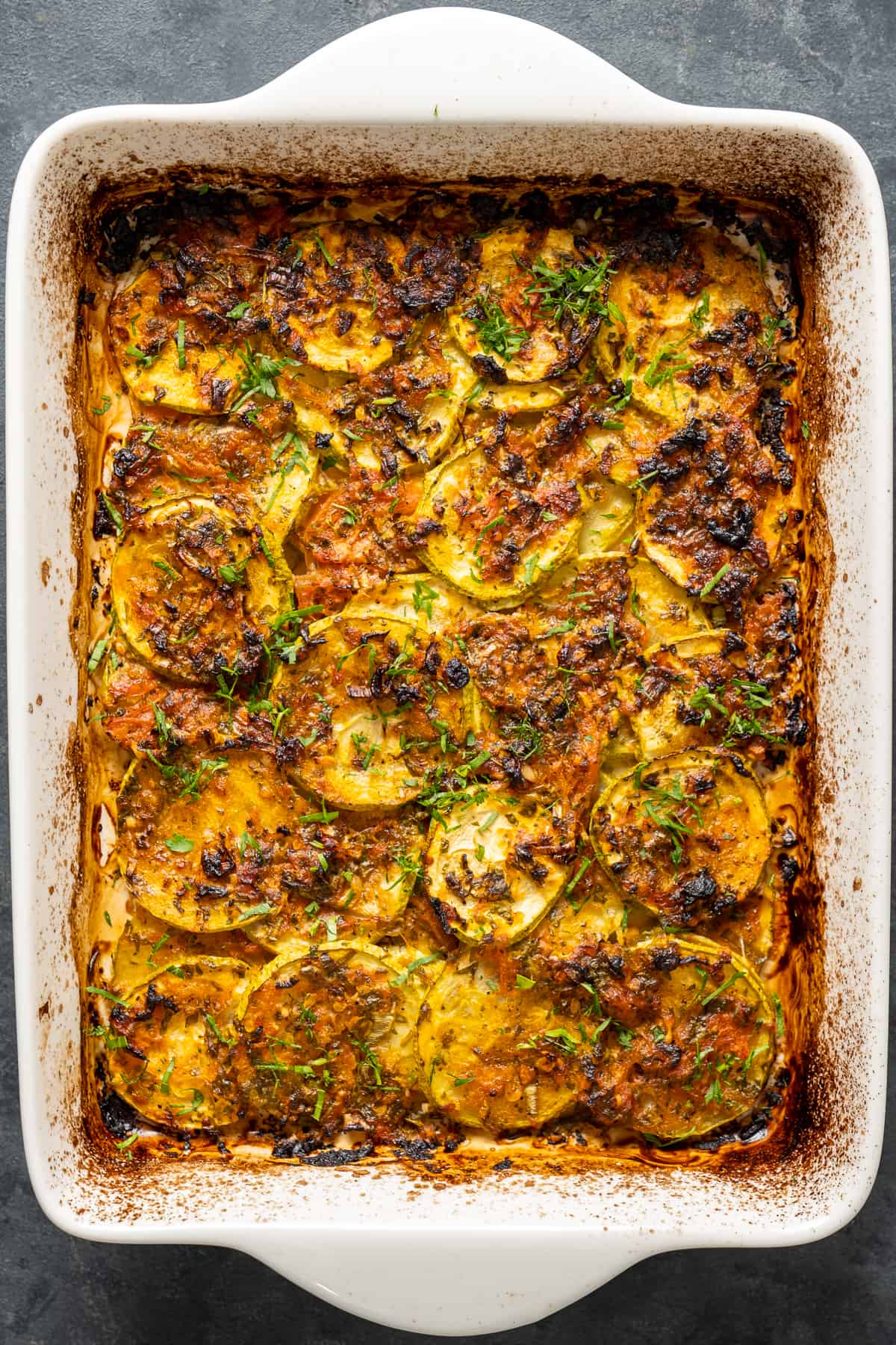 Zucchini tomato casserole with garlic and herbs baked with a golden top in a white baking pan.