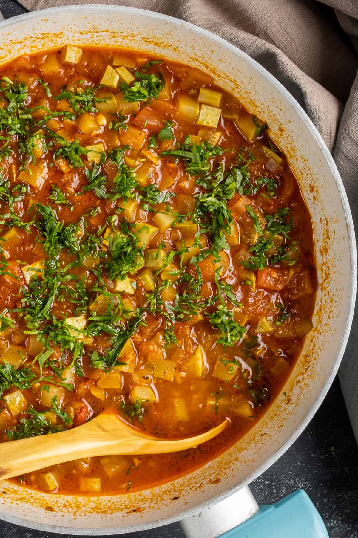 Zucchini stew with tomatoes and herbs in a pan and a wooden spoon in it.