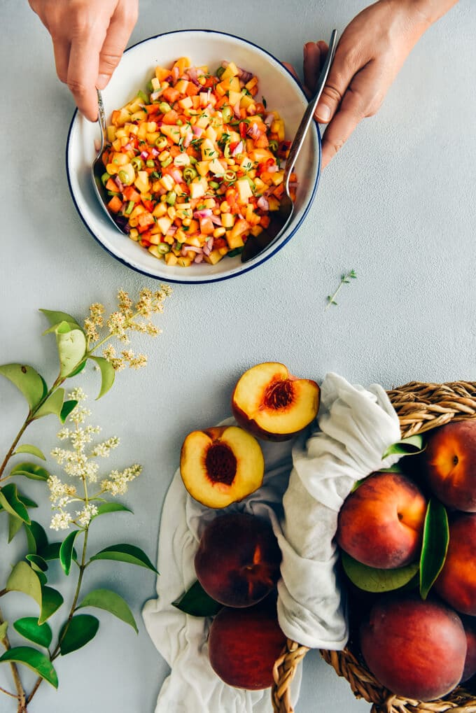 Fresh Corn Peach Salsa is a great recipe to bring summer on your table. Thanks to tangy garden tomatoes, hot peppers and red onion, this is not an overly-sweet salsa. Perfect on chips, chicken, fish or even in sandwiches. #salsa #peachsalsa #salsarecipe #freshpeach #partyfood Hands stirring fresh corn peach salsa in a white bowl