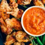 Sugar free bbq sauce with peaches served with chicken wings, thyme and pepper on a black pan