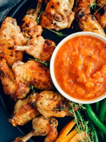 Sugar free bbq sauce with peaches served with chicken wings, thyme and pepper on a black pan