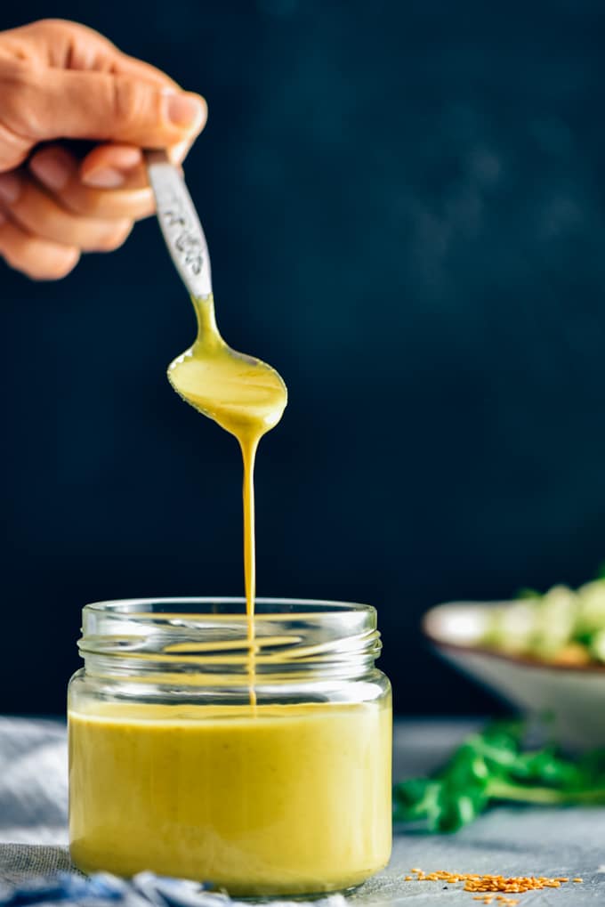 Pouring turmeric tahini dressing with a spoon into a glass jar.