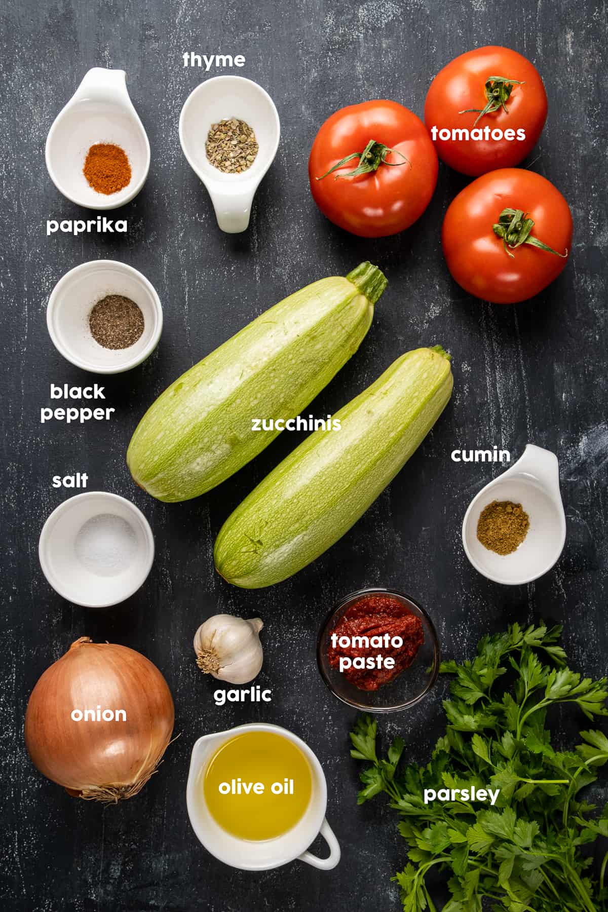 Zucchini, tomatoes, spices, garlic, onion, olive oil, tomato paste, parsley on a dark background.