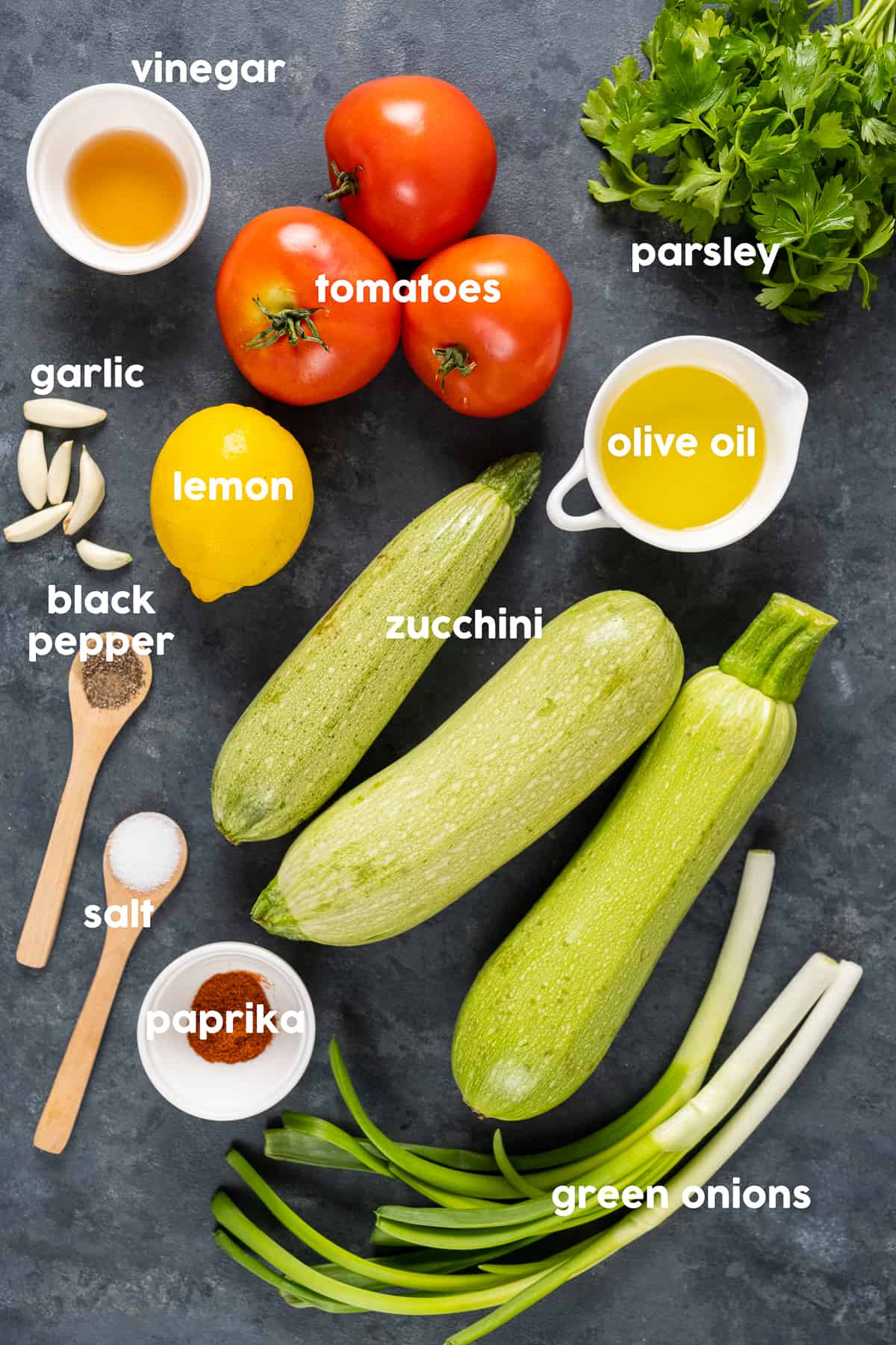 Zucchini, tomatoes, vinegar, parsley, green onions, spices and olive oil on a dark background.