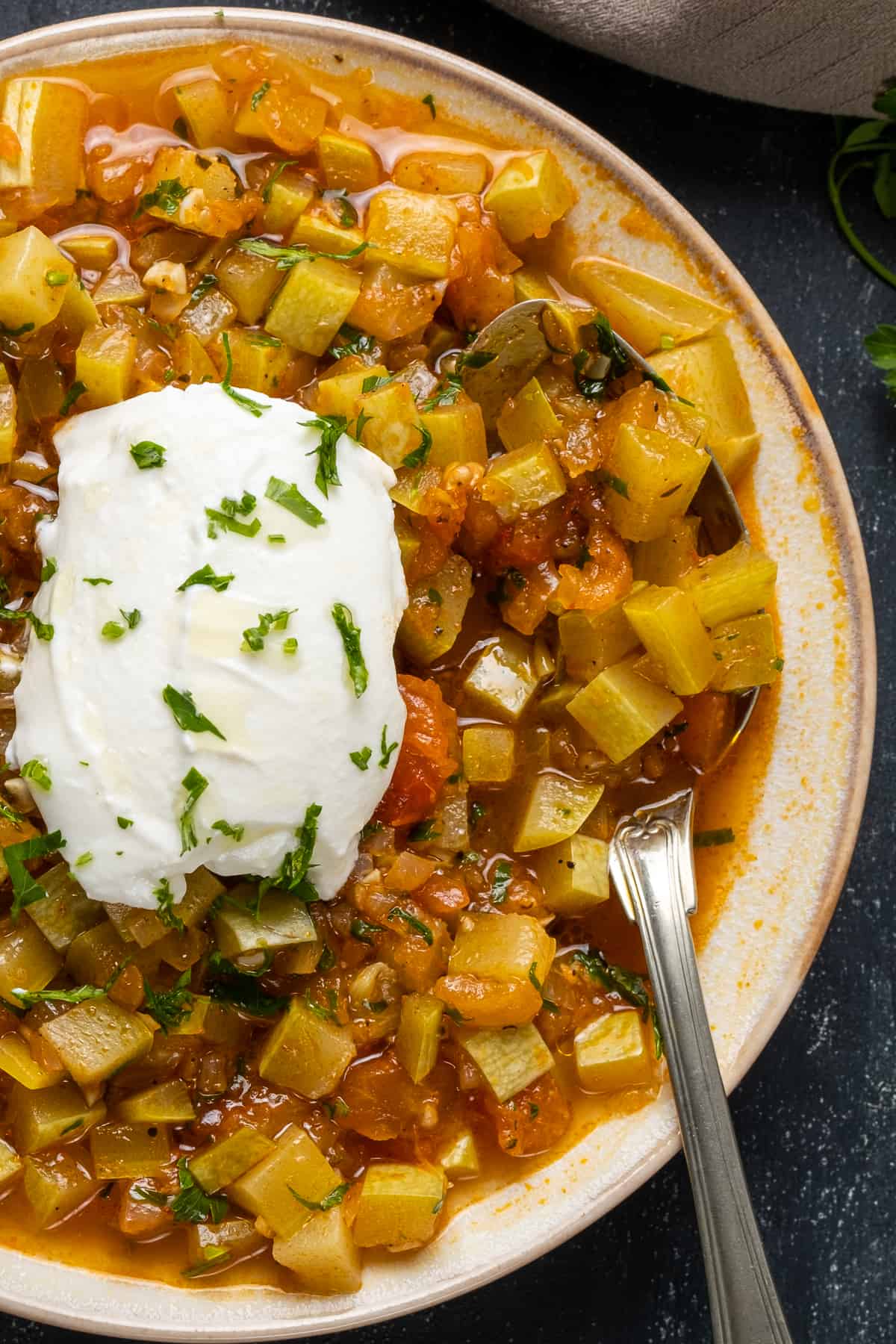 Zucchini stew served in a bowl with a yogurt topping and a fork inside.