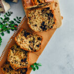 Chocolate chip zucchini bread with walnuts sliced on a wooden board and brown paper on a grey background