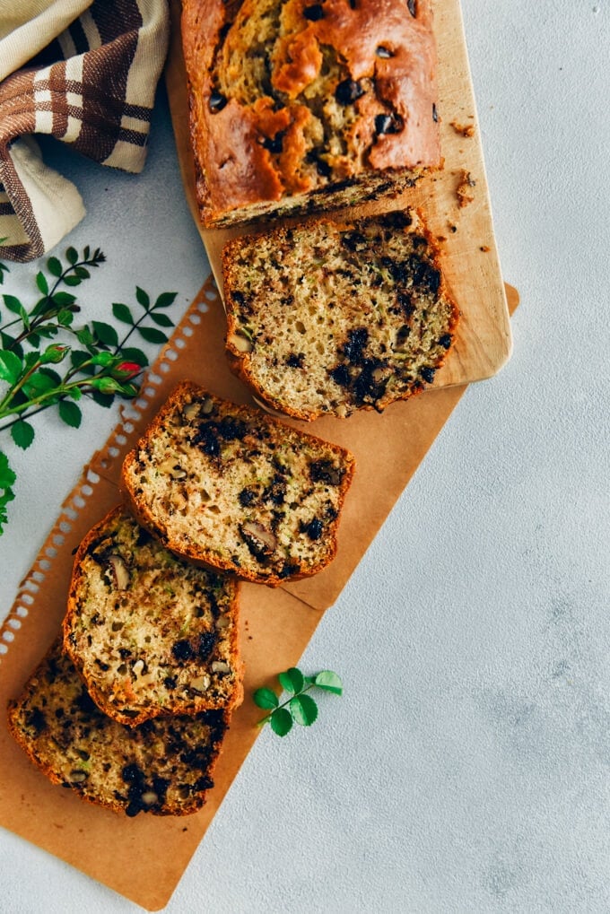 Chocolate chip zucchini bread with walnuts sliced on a wooden board and brown paper on a grey background