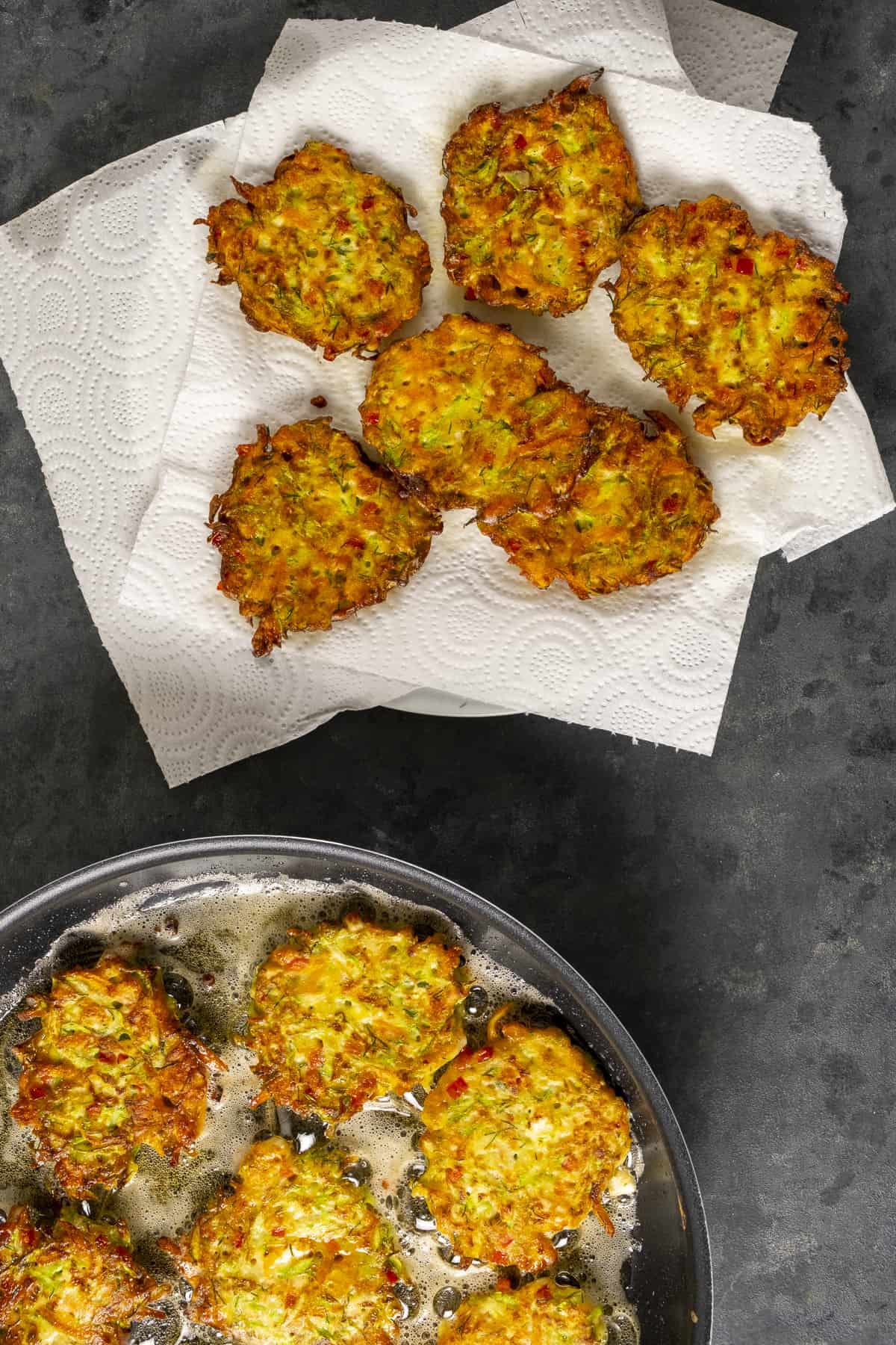 Dome mucver patties frying in a pan and the fried ones are placed on paper towel.