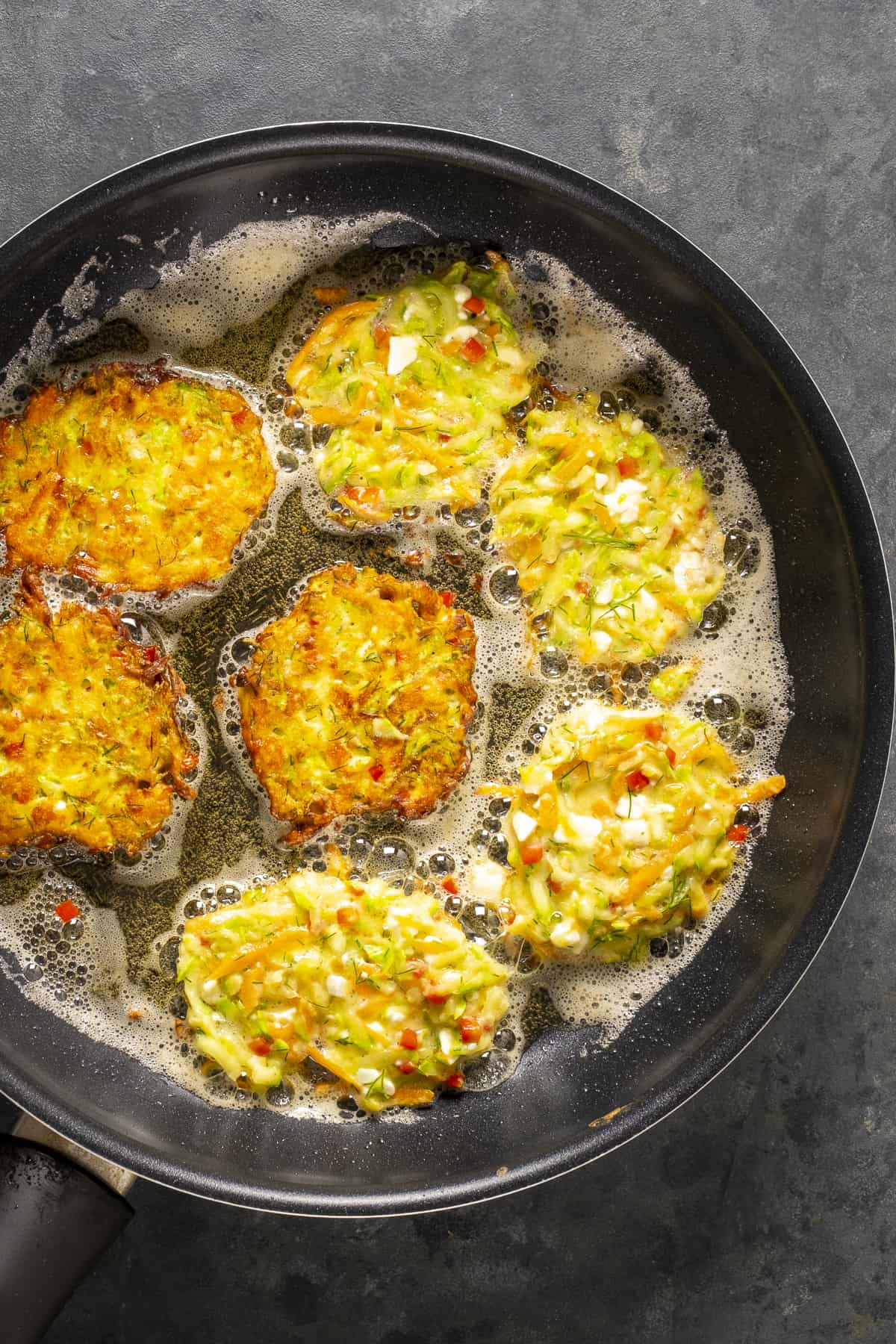 Mucver patties frying in a large frying pan.