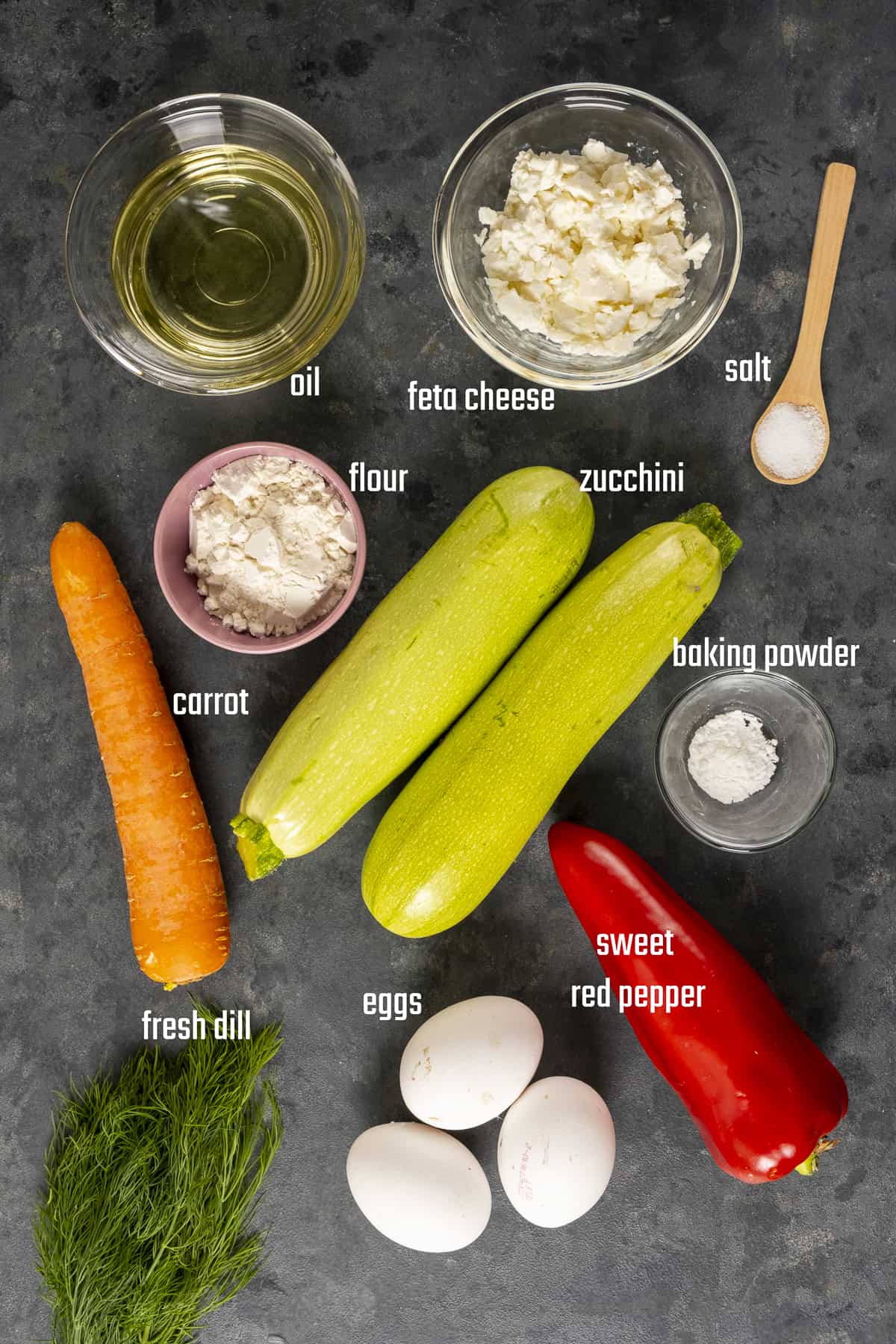 Zucchini, carrots, oil, flour, eggs, sweet red peppers, fresh dill, salt, feta cheese photographed on a dark background.