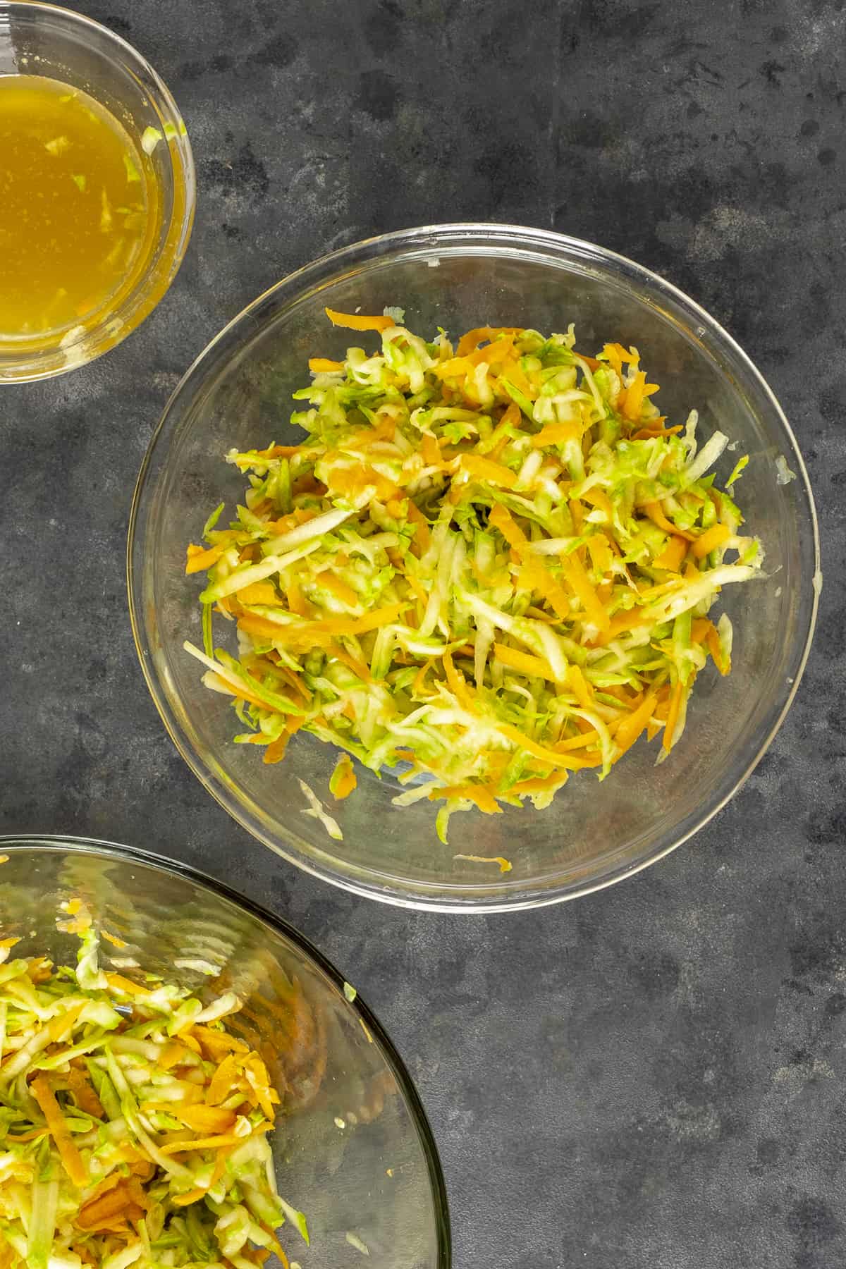 Grated zucchini and carrots in a large glass bowl.