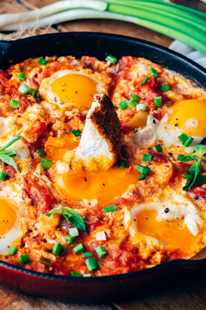 A piece of bread dipped into Turkish egg recipe menemen in an iron skillet