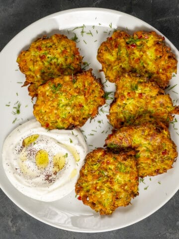 Mucver patties served with yogurt on a white plate.