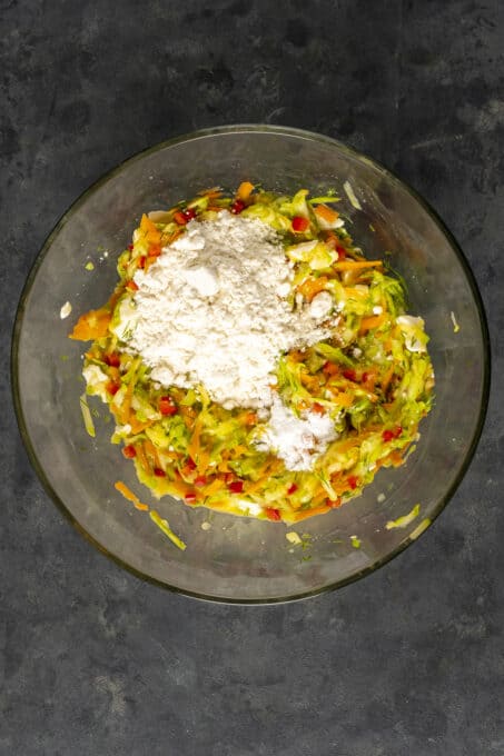 Zucchini fritter mixture in a glass mixing bowl.