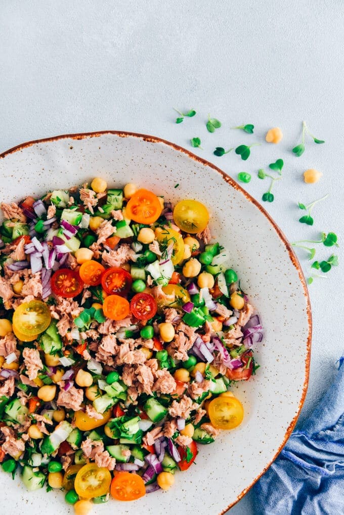 Chickpea tuna salad with tomatoes and cucumbers in a white bowl.