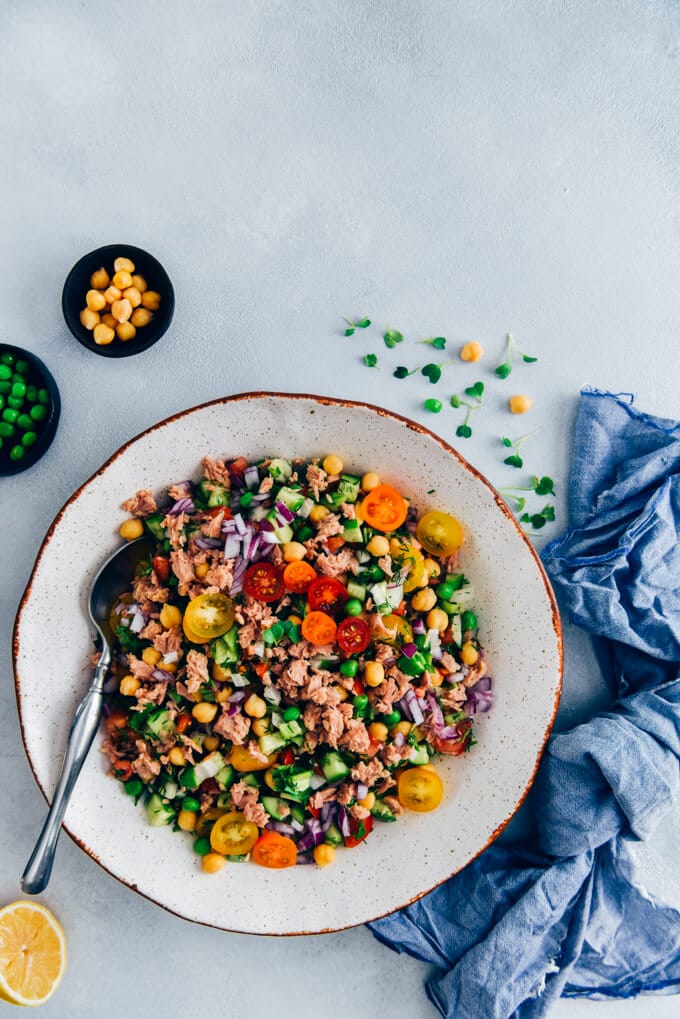 Chickpea Tuna Salad Recipe with a shallot vinaigrette is full of amazing flavors. Packed with protein, fibre and fresh ingredients, this salad is healthy, tasty and keeps you full until dinner time. #tunasalad #chickpeasalad #healthyeating Chickpea tuna salad with cucumbers, onion and tomatoes in a white bowl