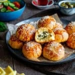 Golden brown pogaca with sesame seeds, one cut open showing a feta and herb filling, served with tea, olives, and cheese.