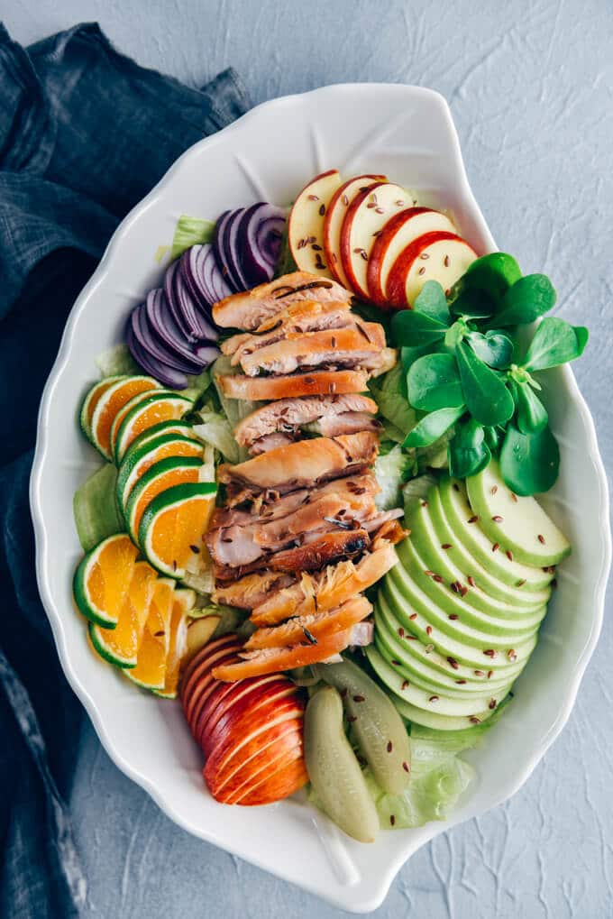 Chicken salad with apples, lettuce, purslane, orange slices in a white salad bowl.